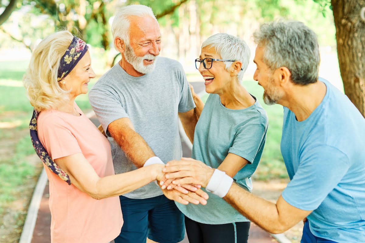 Group of Laughing Seniors Outside with Their Hands Together_Boca Raton Senior Living