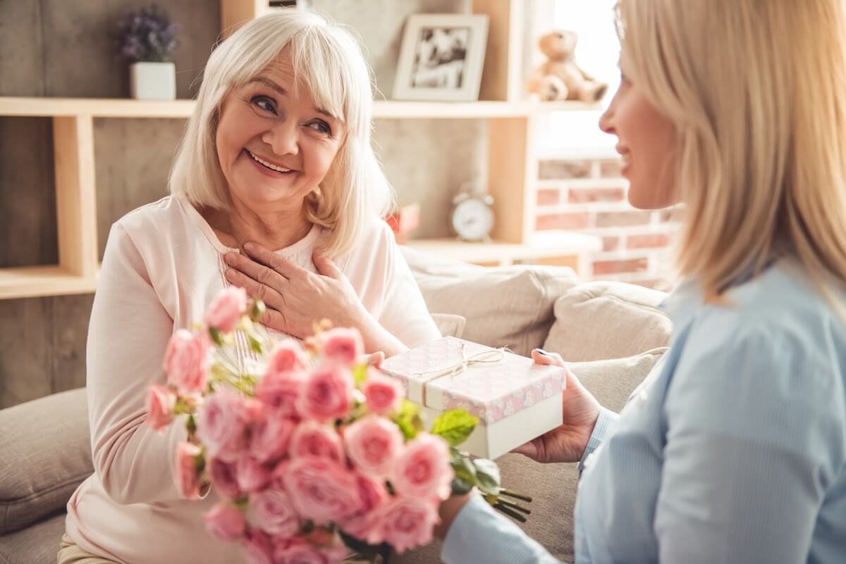 Celebrating Mother’s Day with Mom in Assisted Living Smiling elderly mom receiving flowers on Mothers Day