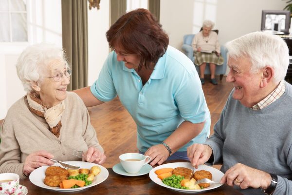 Couple of seniors being served their meal by a caregiver Couple of seniors being served their meal by a caregiver